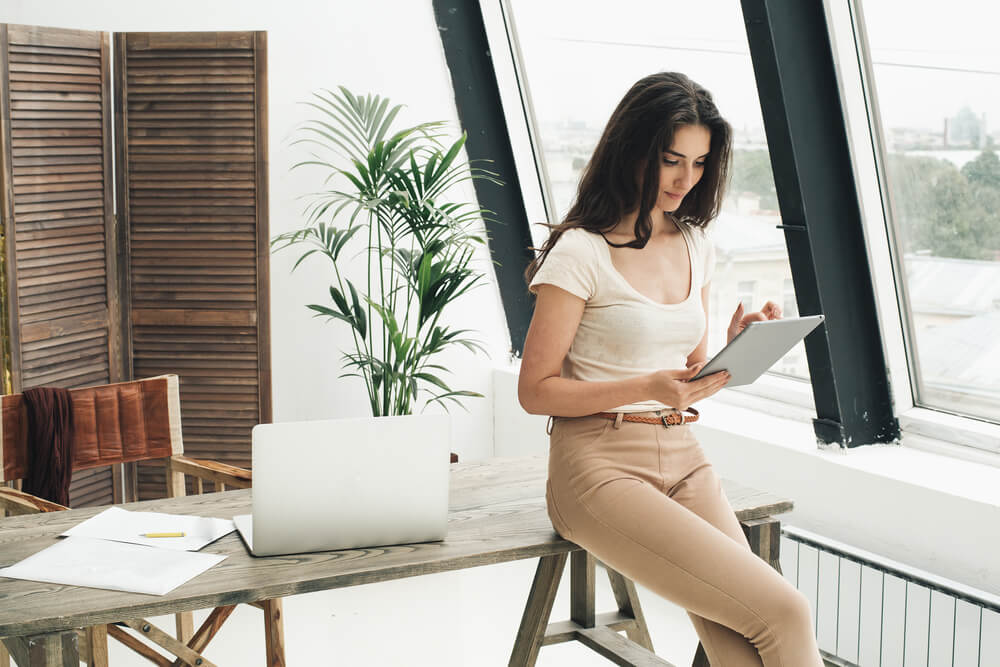 Woman sitting on desk looking at tablet